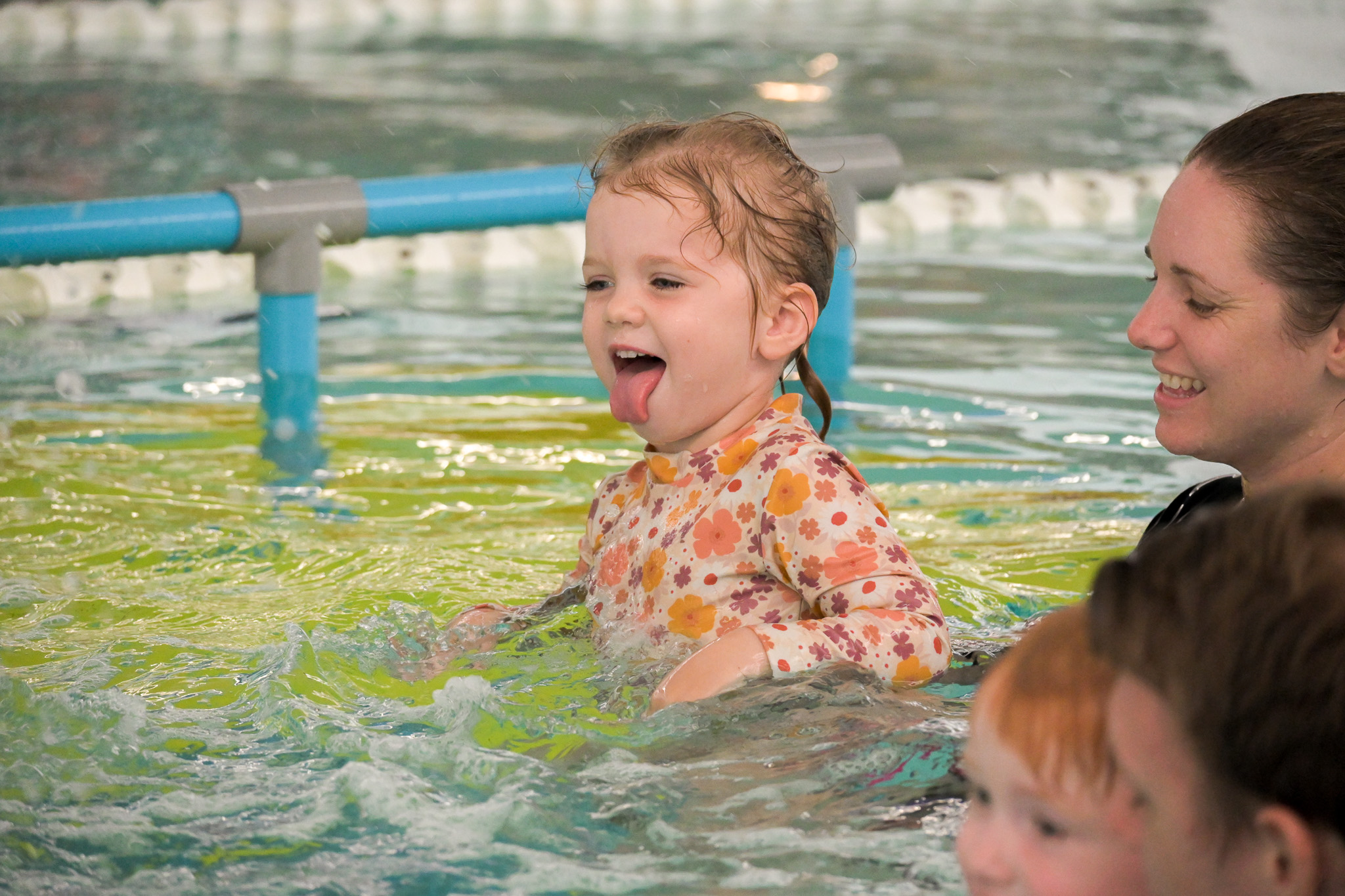 Little girl pokes her tongue out smiling in the pool during a swimming lesson