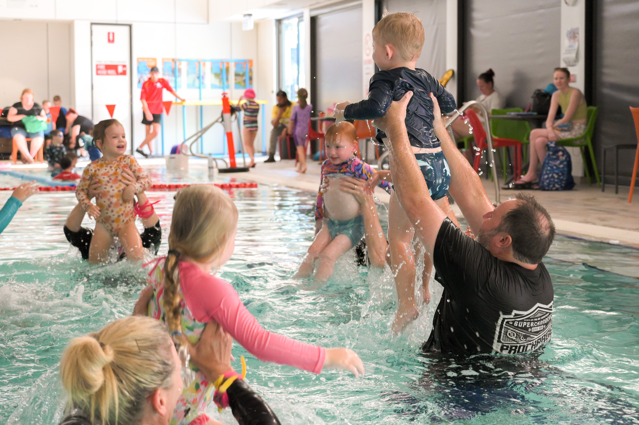 Parents raise their children out of the water creating a big splash