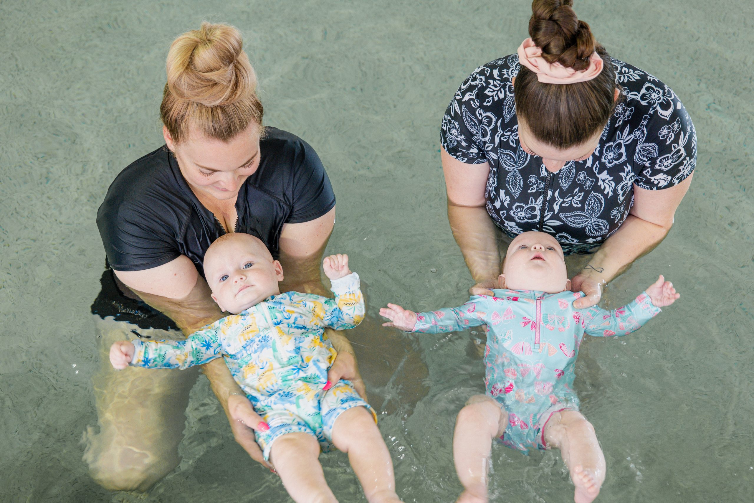 Two mums each hold their babies floating on the water