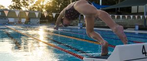 Teenage swimmer dives off a block in the outdoor pool at Logan North Aquatic Centre